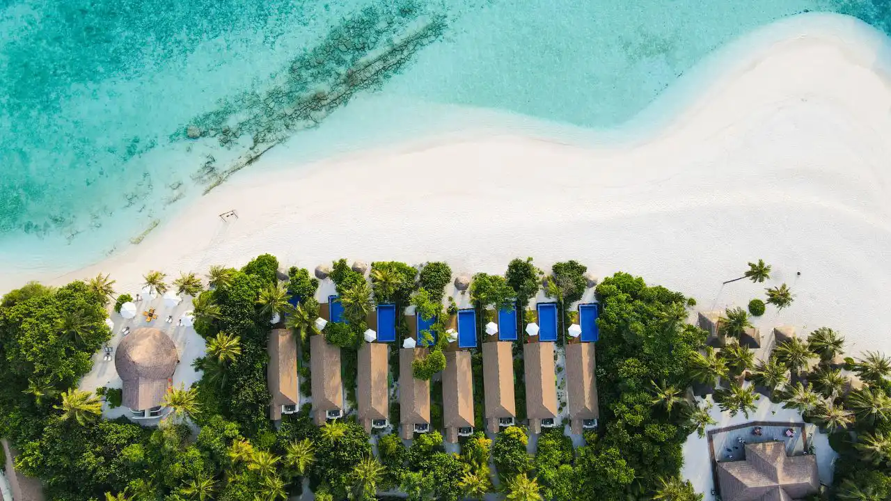 Vista aerea di Reethi Faru Resort Maldives con spiaggia bianca, laguna turchese e vegetazione tropicale